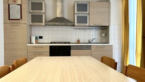 A modern kitchen with a large dining table, built-in cabinets, a stove, and a dishwasher. - R003 - Recanati, delightful three-room apartment in the center (Recanati)