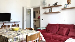 A living room with a red sofa, a dining table with chairs, a TV, and wooden shelves with decorative items. - SE096 - Senigallia, comfortable two-room apartment facing the sea (Senigallia)