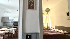 A room with a bed, a dining area with a table and chairs, a kitchen area, and a wall with a religious icon. - SE096 - Senigallia, comfortable two-room apartment facing the sea (Senigallia)