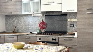 A kitchen with a stove, oven, microwave, and a table with a floral tablecloth. - SE096 - Senigallia, comfortable two-room apartment facing the sea (Senigallia)