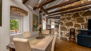 Un espace repas avec une longue table, des chaises, un mur en pierre et une cuisine en arrière-plan.