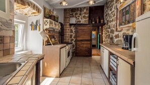 Une cuisine avec un mur en pierre, des armoires en bois et des ustensiles de cuisine suspendus.