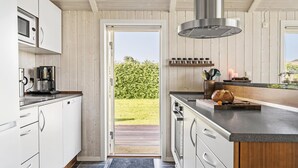 A modern kitchen with wooden paneling, a stainless steel range hood, and a view of a garden through an open door. - Stunning home in Haderslev with WiFi (Haderslev)