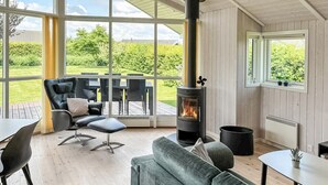 A cozy room with a fireplace, a sofa, a dining table, and a view of a garden through large windows. - Stunning home in Haderslev with WiFi (Haderslev)