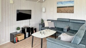 A modern living room with a grey sofa, a white coffee table, and a flat-screen TV mounted on the wall. There is a bookshelf with books and decorative items, and a small potted plant on the floor. - Stunning home in Haderslev with WiFi (Haderslev)