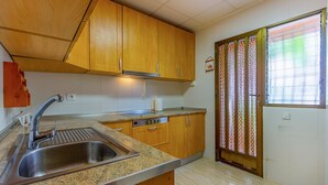 Une cuisine avec des meubles de rangement en bois, un évier en acier inoxydable et une fenêtre agrémentée de stores décoratifs.