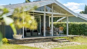 Une terrasse couverte avec des sièges d’extérieur, un pot de fleurs et une haie en arrière-plan.