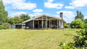 Une maison moderne dotée d’une grande véranda, d’une cheminée et d’une pelouse bien entretenue.