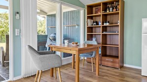 Un coin repas avec une table et des chaises en bois, une bibliothèque intégrée et une vue sur un espace extérieur accessible par une porte vitrée, où se trouve un barbecue.