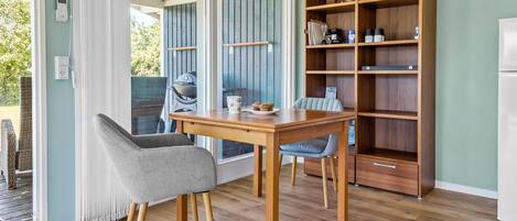 Un comedor con mesa y sillas de madera, una estantería empotrada y vistas a un espacio exterior con una parrilla.