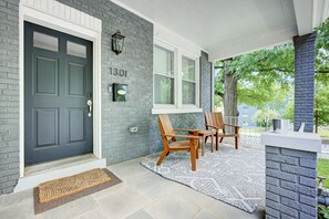 A house with a dark grey door, a number '1301' on the wall, a covered porch with two wooden chairs and a table, and a brick wall. - DC`s premier group home 5 bedrooms, 11 guests, EV charging, free parking (Washington)