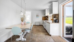 A modern kitchen with white cabinets, a dining area with a table and chairs, and a view of a green field through a door. - 4 bedroom awesome home in Frørup (Frørup)