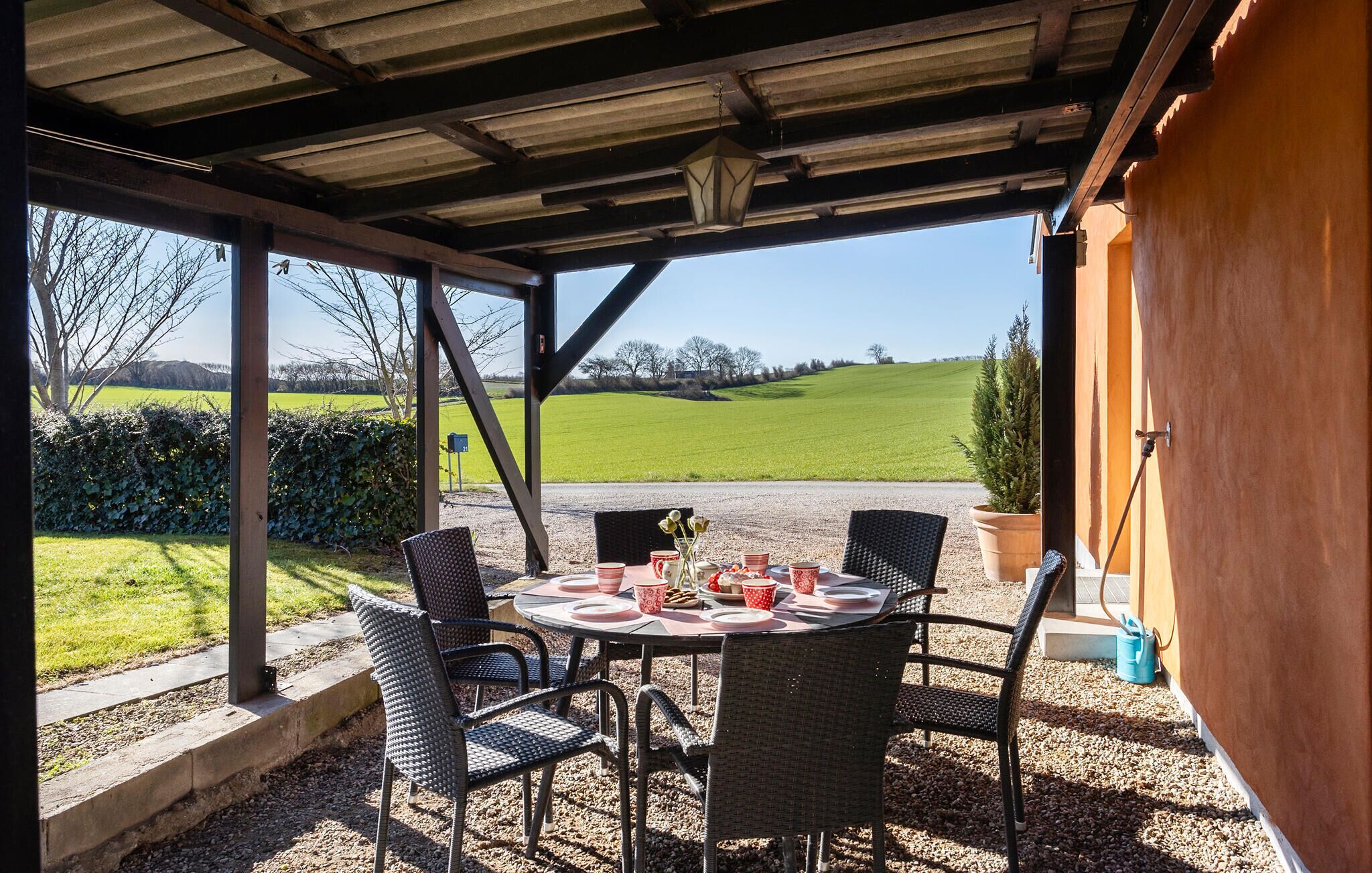 A covered outdoor dining area with wicker chairs and a table set for four, overlooking a green field.