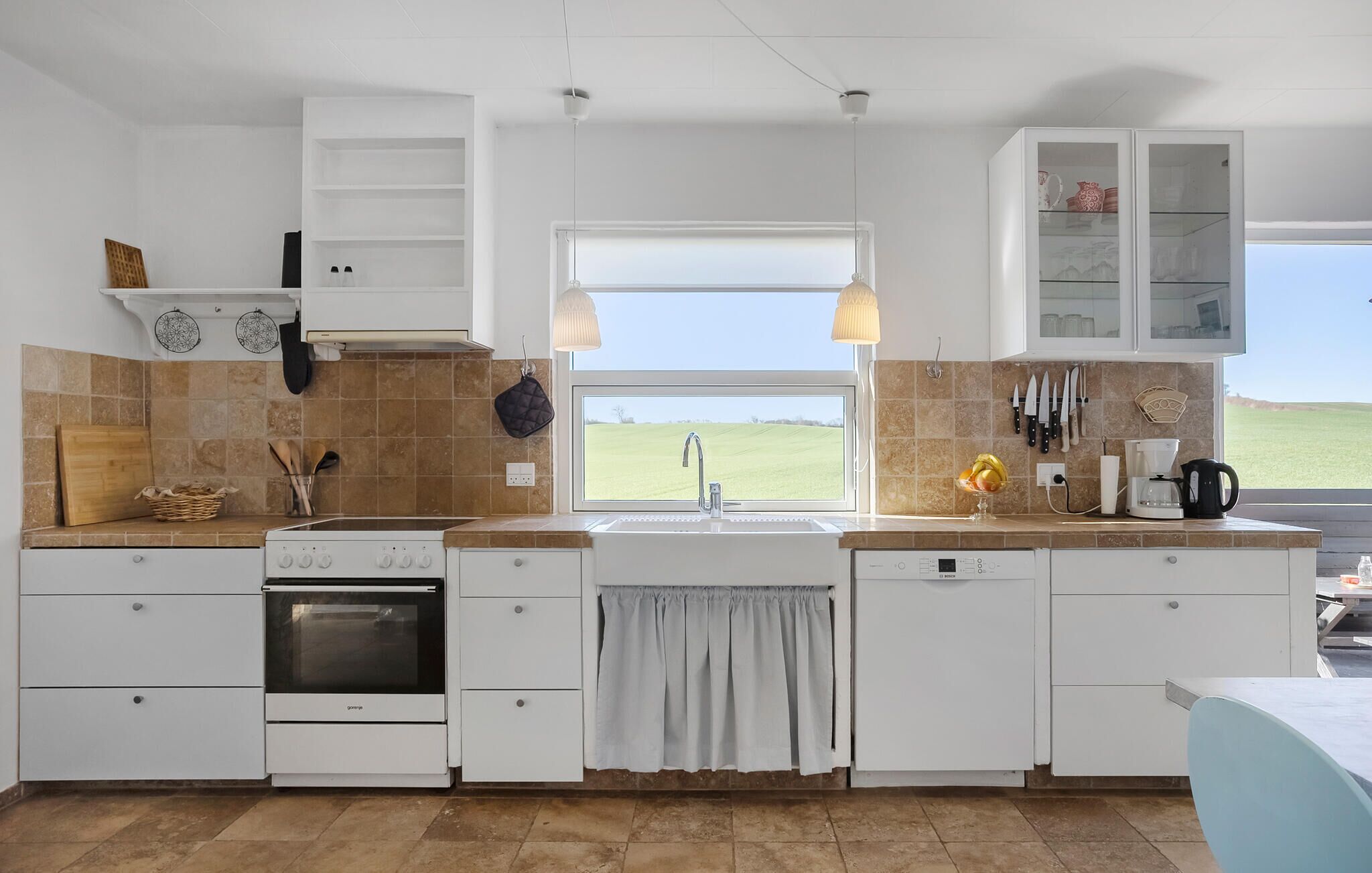 Une cuisine avec des meubles blancs, une cuisinière, un évier donnant sur un beau paysage et une fenêtre.