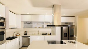Une cuisine moderne avec des meubles blancs, des appareils en acier inoxydable et un îlot central doté d’un évier.