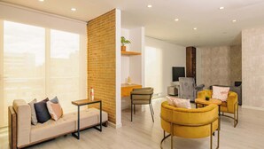Un salon moderne avec un canapé, des fauteuils jaunes, une table basse et un téléviseur.