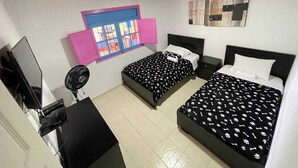 A bedroom with two beds, a desk with a computer, a fan, and a window with pink shutters. - finca el arrullo (Armenia)