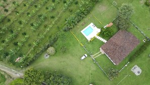 An aerial view of a property with a swimming pool, a tennis court, and a fenced area with trees. - finca el arrullo (Armenia)