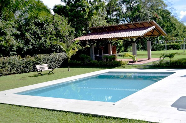 A rectangular swimming pool with a tiled deck, surrounded by a well-maintained lawn and a gazebo with a tiled roof. - finca el arrullo (Armenia)
