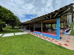 A covered outdoor seating area with a tiled floor and a grassy lawn. - finca el arrullo (Armenia)