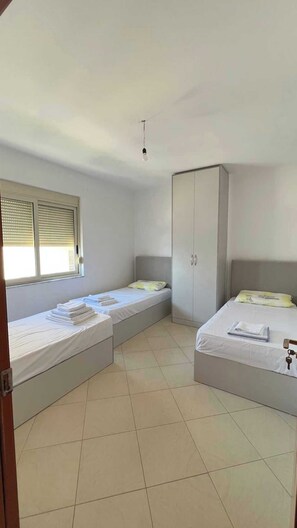 A room with two beds, a wardrobe, and a window with blinds.