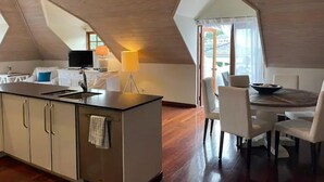 A modern kitchen with a central island, a dining area with a round table and chairs, and a large window providing natural light.