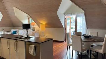 A modern kitchen with a central island, a dining area with a round table and chairs, and a large window providing natural light.