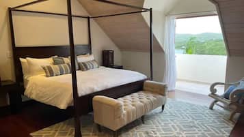 A four-poster bed with a bench, a patterned rug, and a view of the outdoors.