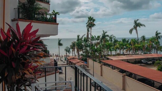 Ein Balkon mit Blick auf den Strand, Palmen und einen Parkplatz.