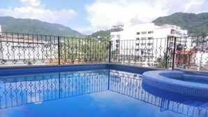 Ein Schwimmbecken mit Metallzaun, umgeben von Gebäuden und Bergen.