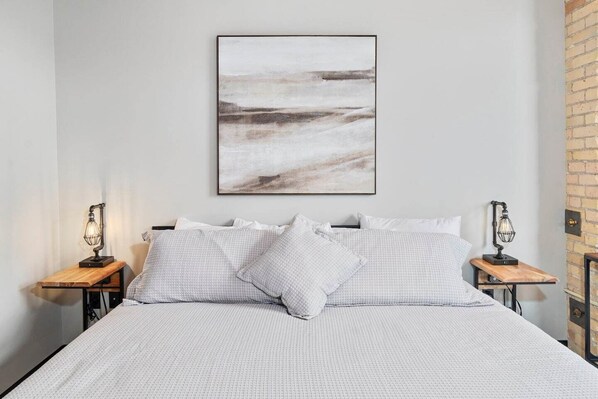 A modern bedroom with a large bed, white bedding, and two bedside tables with lamps.