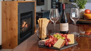 Una mesa de comedor con una botella de vino, copas y una tabla de fiambres con queso, uvas y embutidos.