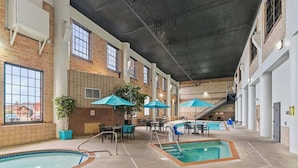 Un área de piscina interior con varias piscinas, zonas de estar y sombrillas.