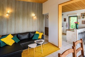 A modern living room with a black leather sofa, yellow and green cushions, a small white table, and a yellow rug.