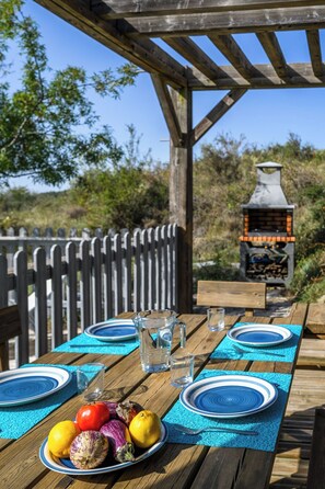 An outdoor dining area with a wooden table set for two, a grill in the background, and a wooden fence surrounding the space.