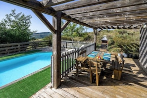 Een houten terras met een zwembad, een barbecue en een zithoek.