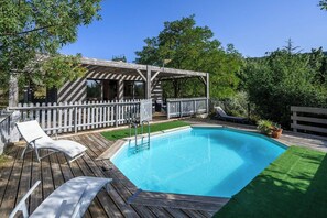 A wooden deck with a swimming pool, a covered seating area, and a white picket fence.