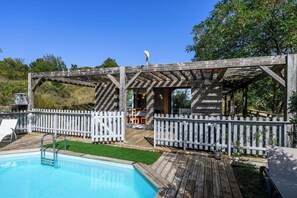 A wooden deck with a pool, white picket fence, and a covered seating area.