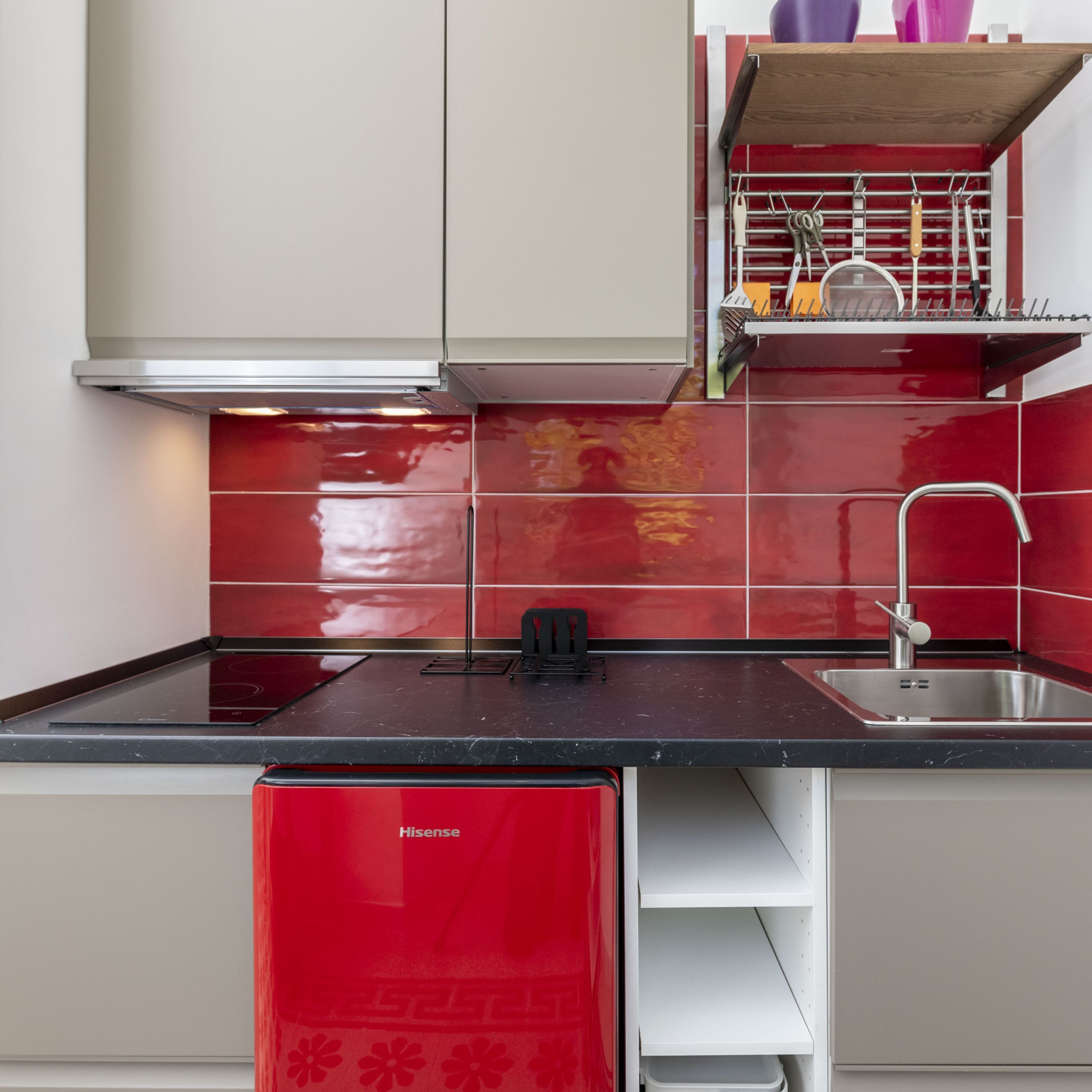 A kitchen with red and white cabinetry, a black countertop, and a stainless steel sink.