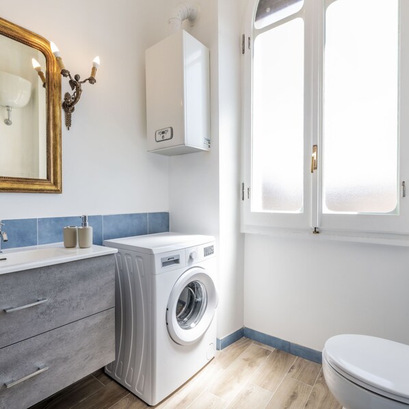 A modern bathroom with a washing machine, a mirror with a gold frame, and a window. - Trastevere 900 Liberty (Rome)