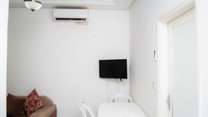 Una habitación con cama, televisión montada en la pared, aire acondicionado, sofá con cojín y una puerta.