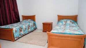 Un dormitorio con dos camas de madera, una mesita de noche de madera y una cortina roja.