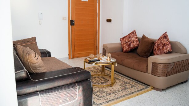 Una sala de estar con un sofá de cuero marrón, un sofá beige con cojines estampados y una pequeña mesa redonda de centro con una alfombra.