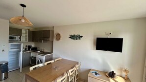 Une cuisine compacte dotée d’appareils électroménagers modernes, un coin repas avec une table et des chaises en bois, et un petit téléviseur fixé au mur.