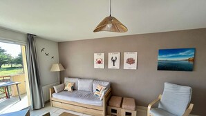 Une pièce comprenant un canapé, un fauteuil, une table, un luminaire suspendu et des œuvres d’art murales.