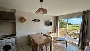 Une pièce comprenant une table à manger, des chaises, un lave-linge, un téléviseur et un balcon avec vue sur l’extérieur.