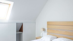 Une chambre avec un plafond en pente, une tête de lit en bois, une lampe de chevet et une fenêtre.