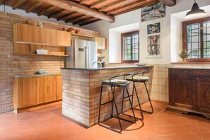 A kitchen with wooden cabinets, a brick island, bar stools, and a window with artwork.
