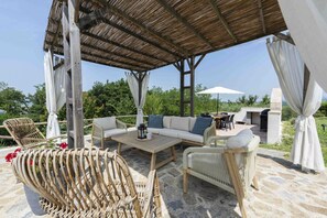 Une terrasse extérieure aménagée avec des meubles en osier, une table en bois et un espace couvert doté d’un toit de chaume.