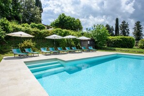 A swimming pool with lounge chairs and umbrellas, surrounded by greenery and trees.